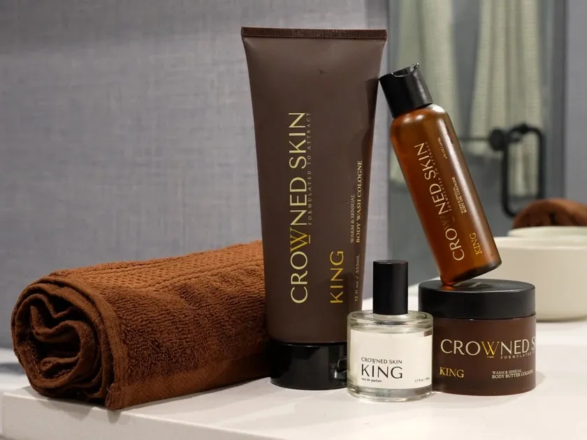 A King body wash tube, a bottle, a jar and a bottle of eau de parfum beside a folded brown towel